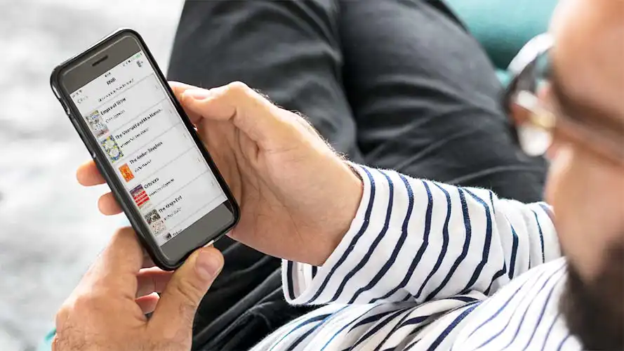 User holding a smartphone with book list onscreen.